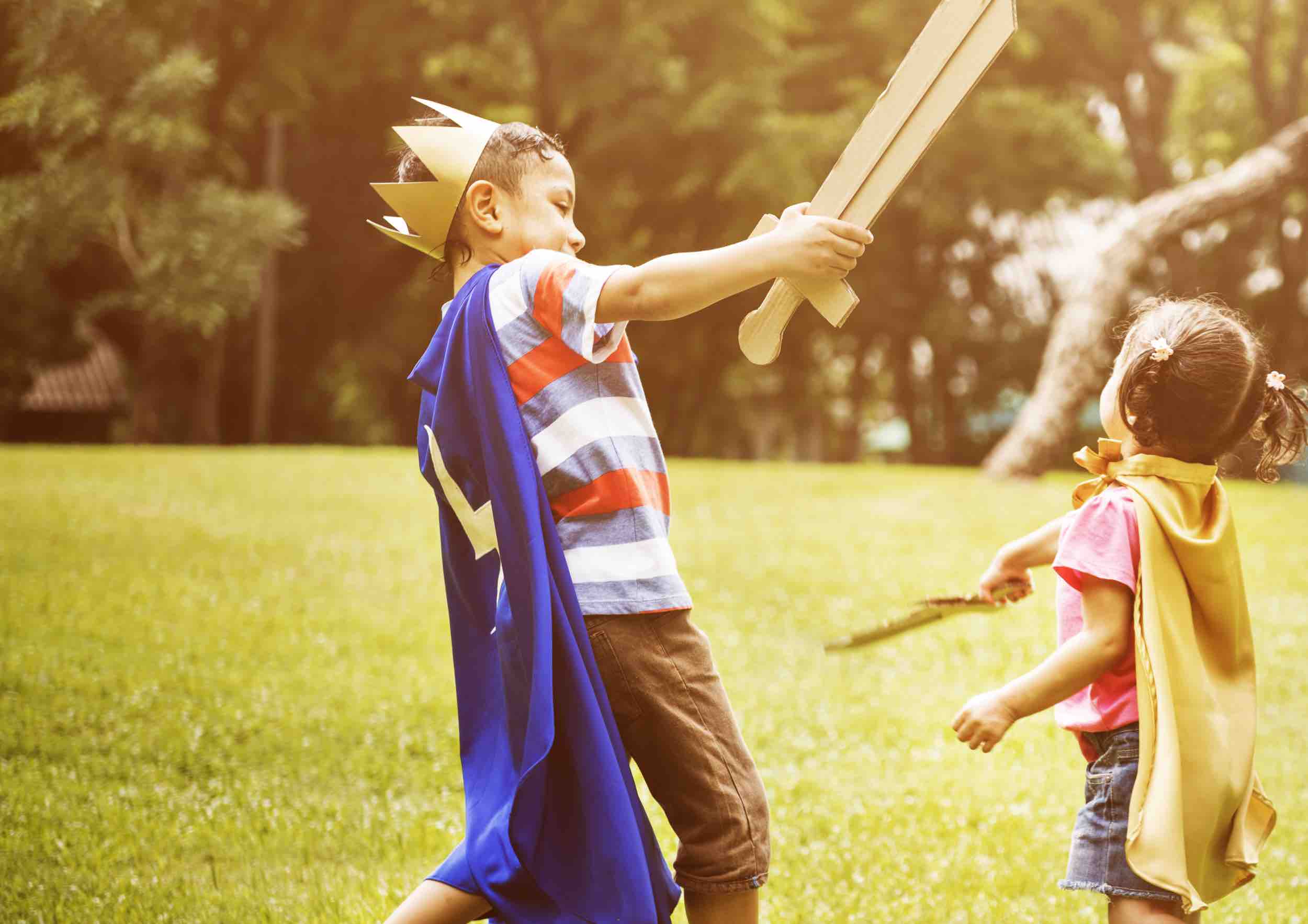 Boy with cardboard sword and king's crown and cape outside with little girl also with sword